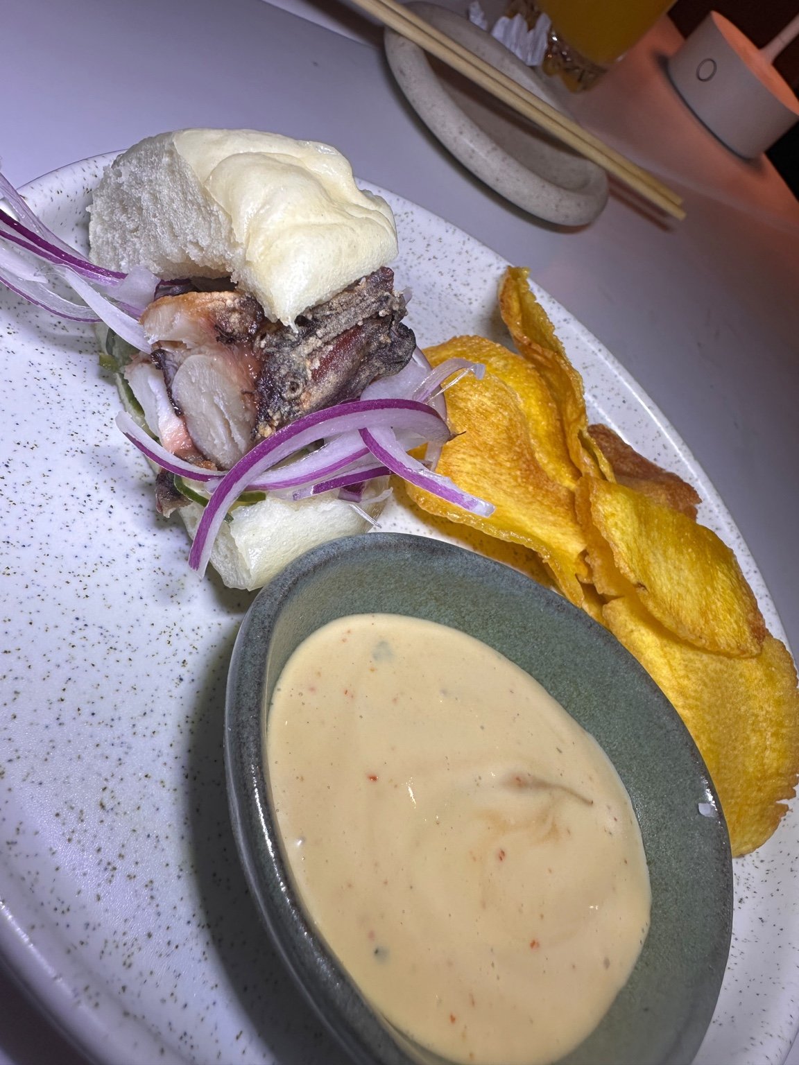Bun de Polvo com cebola roxa, acompanhado de molho e chips.